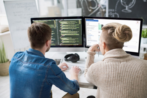 Two developers sitting in front of two computer monitors inspecting code.